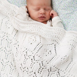 K&ouml;nnte beinhalten: Eine wei&szlig;e geh&auml;kelte Babydecke mit einem zarten Spitzenmuster. Die Decke liegt &uuml;ber einem schlafenden Baby.