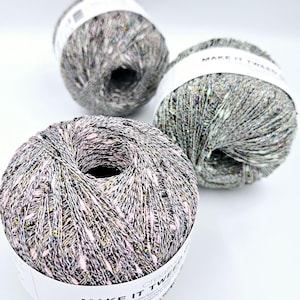 May include: Three balls of yarn in different colors, each with a white label that says "Make It Tweed" and "Creative Collection" with a description of the yarn. The yarn is a tweed blend with a speckled appearance.