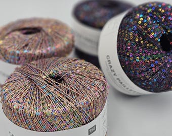 May include: Close-up of three skeins of yarn with colorful sequins woven into the thread. The yarn is labeled "CRAZY PAILLETTES" and "creative".