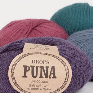 May include: Close-up of several balls of Drops Puna Uni Colour yarn in shades of purple, teal, and mauve. The front ball displays a label with the brand name and fiber content, 100% alpaca. The yarn is described as soft and warm.