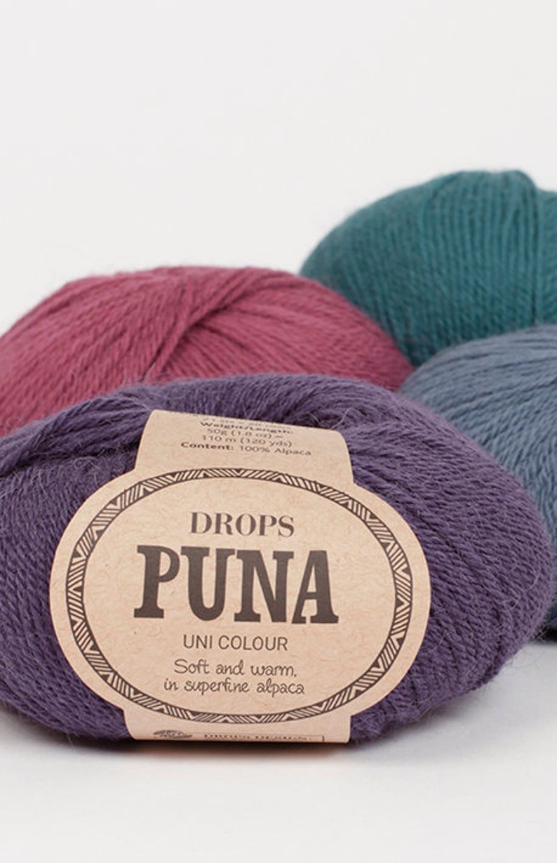 May include: Close-up of several balls of Drops Puna Uni Colour yarn in shades of purple, teal, and mauve. The front ball displays a label with the brand name and fiber content, 100% alpaca. The yarn is described as soft and warm.