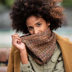May include: A person wearing a brown and green knitted scarf with a brown jacket and a green shirt.