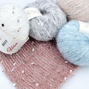 Könnte beinhalten: Vier Knäuel Garn mit Pailletten in Weiß, Grau, Hellblau und Rosa. Das Garn ist weich und flauschig, und die Pailletten sind im Garn verteilt.