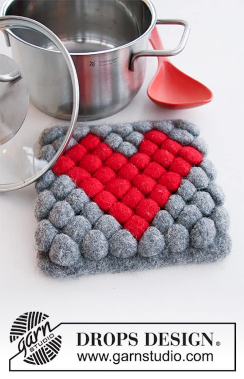 May include: A gray and red heart-shaped pot holder made of felt balls. The pot holder is perfect for protecting surfaces from hot pots and pans.