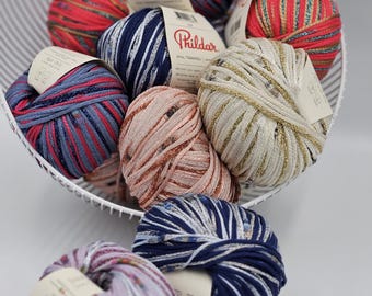 May include: A basket of colorful yarn balls with the brand name "Phildar" on the labels. The yarn is a mix of textures and colors, including pink, blue, gold, and white.