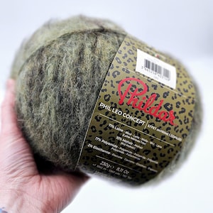 以下が含まれることがあります： ヒョウ柄のラベルが付いた緑と茶色の糸のボール。ラベルには「Phil Leo Concept」と記載されており、糸の組成は71%ウール、10%モヘア、17%ポリアミド、2%エラスタンとなっています。糸の重さは230グラムで、8.11オンスです。