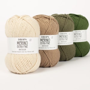 Pode incluir: Quatro novelos de l&atilde; em diferentes tons de bege, castanho e verde. A l&atilde; &eacute; etiquetada como "DROPS MERINO EXTRA FINE UNI COLOUR".