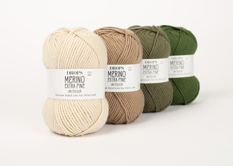 Pode incluir: Quatro novelos de l&atilde; em diferentes tons de bege, castanho e verde. A l&atilde; &eacute; etiquetada como "DROPS MERINO EXTRA FINE UNI COLOUR".