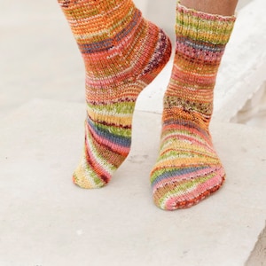 Puede incluir: Un par de calcetines de rayas coloridas con un logotipo de ovillo de lana y el texto "DROPS DESIGN" y "www.garnstudio.com".