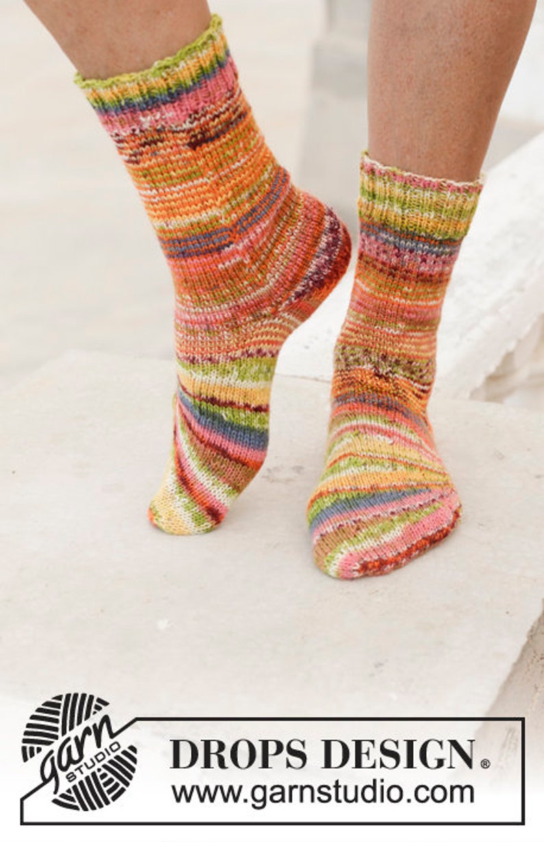 Puede incluir: Un par de calcetines de rayas coloridas con un logotipo de ovillo de lana y el texto "DROPS DESIGN" y "www.garnstudio.com".