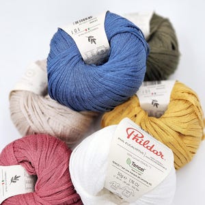 May include: Five balls of yarn in different colors: blue, beige, yellow, red, and white. The white ball has a label that reads "Thildar Phil Eucalyptus 100% Lyocell (TENCEL) 100% Biodegradable Tencel - est une marque de Lenzing AG 50g e 1,76 Oz 90 m - 98 yds - 556 Tex"