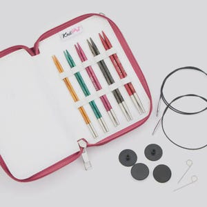 May include: A KnitPro knitting needle set in a pink zippered case. Includes five pairs of interchangeable needles in yellow, teal, pink, grey, and red, two black circular cables, four black end caps, and two small metal tightening pins.