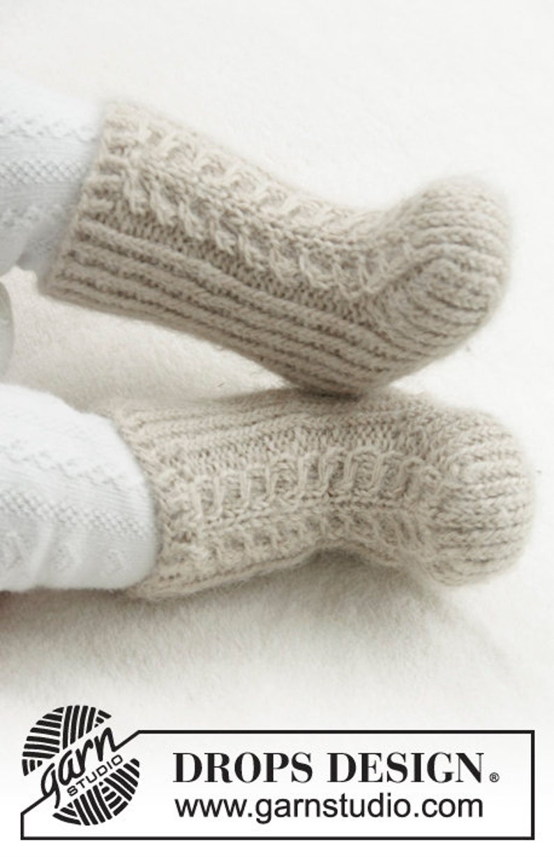May include: Close-up of two light beige knitted socks with a cable knit pattern. The socks are made of a soft, textured yarn and are designed for warmth and comfort. The socks are a neutral color, suitable for various outfits.