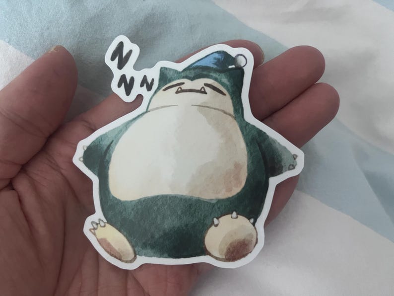 K&ouml;nnte beinhalten: Ein Aufkleber mit einer Aquarellillustration eines schlafenden Snorlax-Charakters. Das Snorlax ist in Gr&uuml;n-, Wei&szlig;- und Braunt&ouml;nen gehalten und tr&auml;gt eine blaue M&uuml;tze. Der Aufkleber hat einen wei&szlig;en Rand und den Text "Zzz".