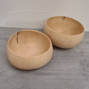 Könnte beinhalten: Zwei natürliche, hellbraune Holzschalen. Die Schalen sind rund und haben eine glatte, leicht strukturierte Oberfläche.
