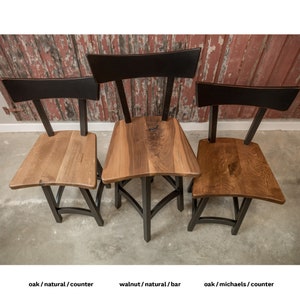 May include: Three wooden chairs with black metal frames. The chairs are made of oak and walnut wood. The chairs are in natural wood finishes. The chairs are in different styles. The chairs are on a concrete floor.