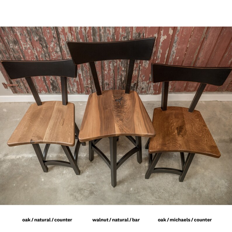 May include: Three wooden chairs with black metal frames. The chairs are made of oak and walnut wood. The chairs are in natural wood finishes. The chairs are in different styles. The chairs are on a concrete floor.