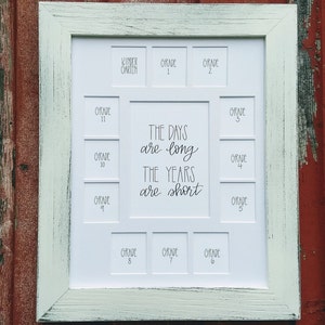 May include: White picture frame with 12 openings for photos. The openings are labeled with the grades Kindergarten through 12. The frame has the text "The days are long, the years are short" written in black cursive.