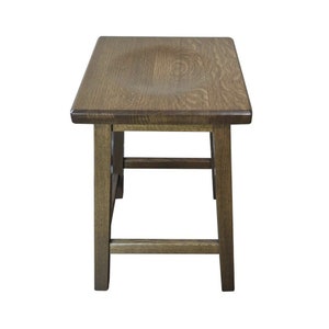 May include: A dark brown wooden stool with a square top and four legs. The stool has a simple design with a single stretcher connecting the legs.