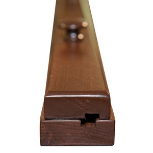 May include: Close-up of a dark brown wooden frame with a decorative knob on the top. The frame is designed to hold a picture or artwork.
