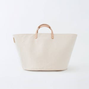 May include: A large, off-white canvas tote bag with brown leather handles and brass accents.
