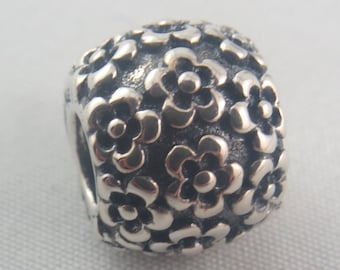 May include: A silver charm bead with a floral design. The bead is round and covered in small, raised flowers.