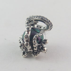 Könnte beinhalten: Silberner Anhänger mit einem Oktopus mit einer grün-schwarzen, schillernden Muschel. Der Oktopus hat einen Ring auf dem Kopf.