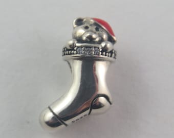 May include: Silver charm in the shape of a Christmas stocking with a teddy bear wearing a red Santa hat peeking out of the top. The stocking is decorated with clear cubic zirconia stones.