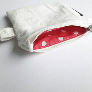 May include: A white zippered pouch with a red and white polka dot lining. The pouch has a small loop handle.