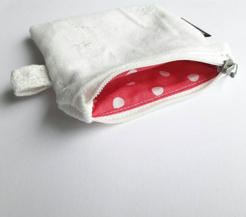 May include: A white zippered pouch with a red and white polka dot lining. The pouch has a small loop handle.