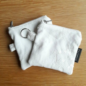 May include: Two white zippered pouches with a key ring. One pouch is plain white corduroy and the other has white embroidery and sequins. The pouch with the embroidery has a black label that says "JESSIESTYLE".