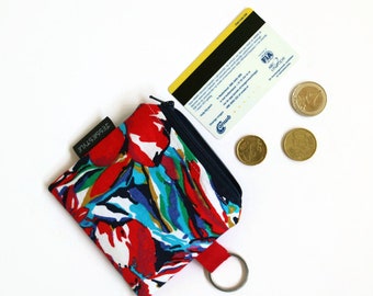 May include: A small zippered pouch with a colorful abstract floral print in shades of red, blue, green, and white. The pouch has a black zipper and a silver key ring attached.