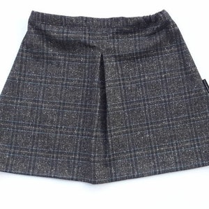 May include: A gray plaid skirt with a pleated front. The skirt has a black waistband and a small black label on the right side.