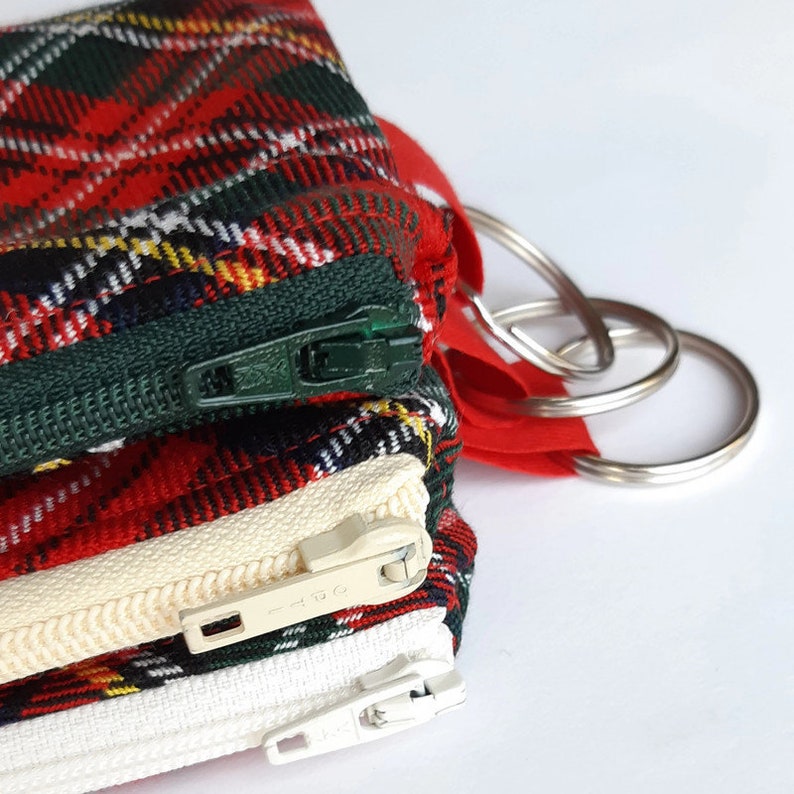 May include: A set of three small zippered pouches with a red, green, and white plaid pattern. The pouches are attached to a silver key ring.