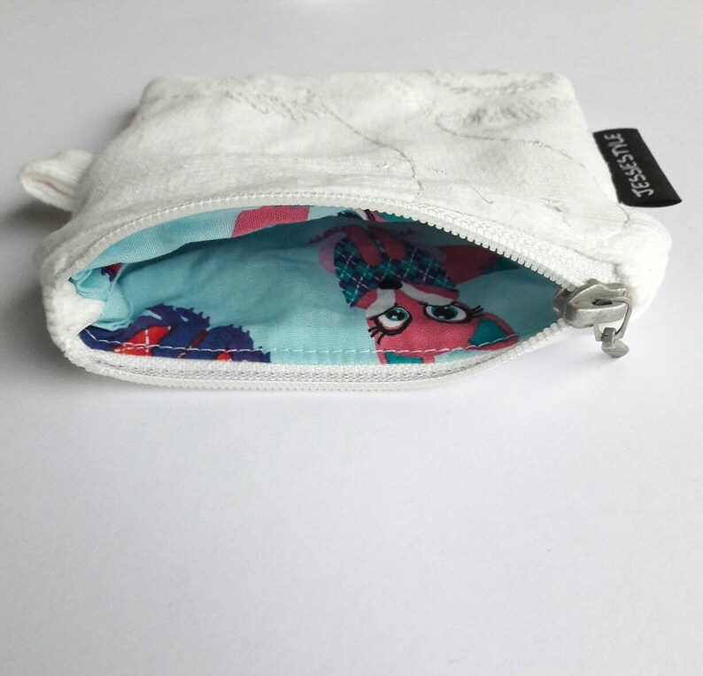 May include: White zippered pouch with a blue and pink patterned lining. The pouch has a small tag that says "JESSESTYLE".