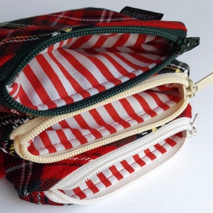 May include: A red, green, and yellow plaid zippered pouch with three compartments. Each compartment has a white and red striped lining.