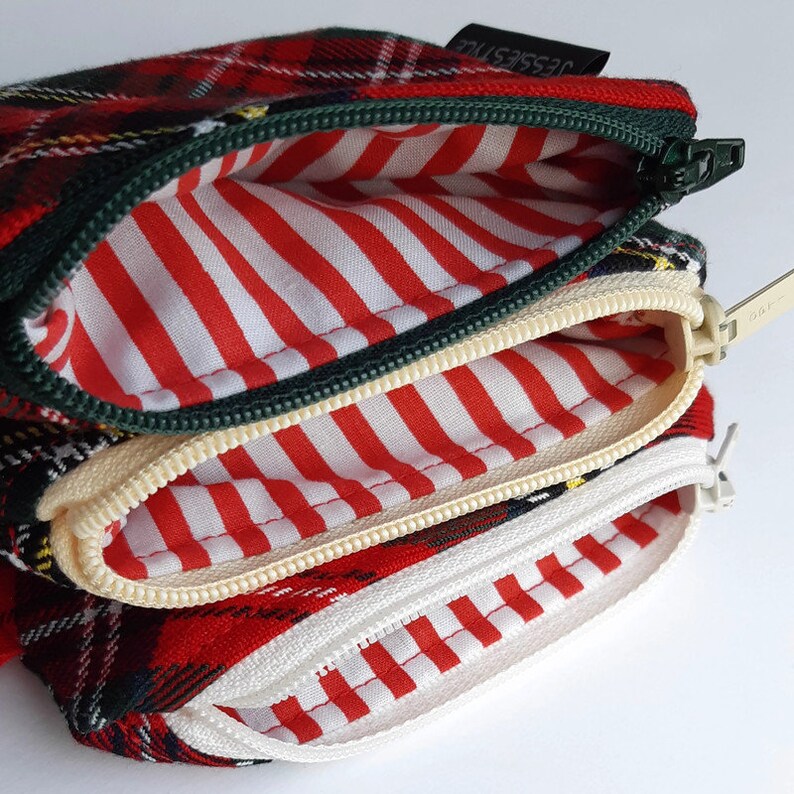 May include: A red, green, and yellow plaid zippered pouch with three compartments. Each compartment has a white and red striped lining.
