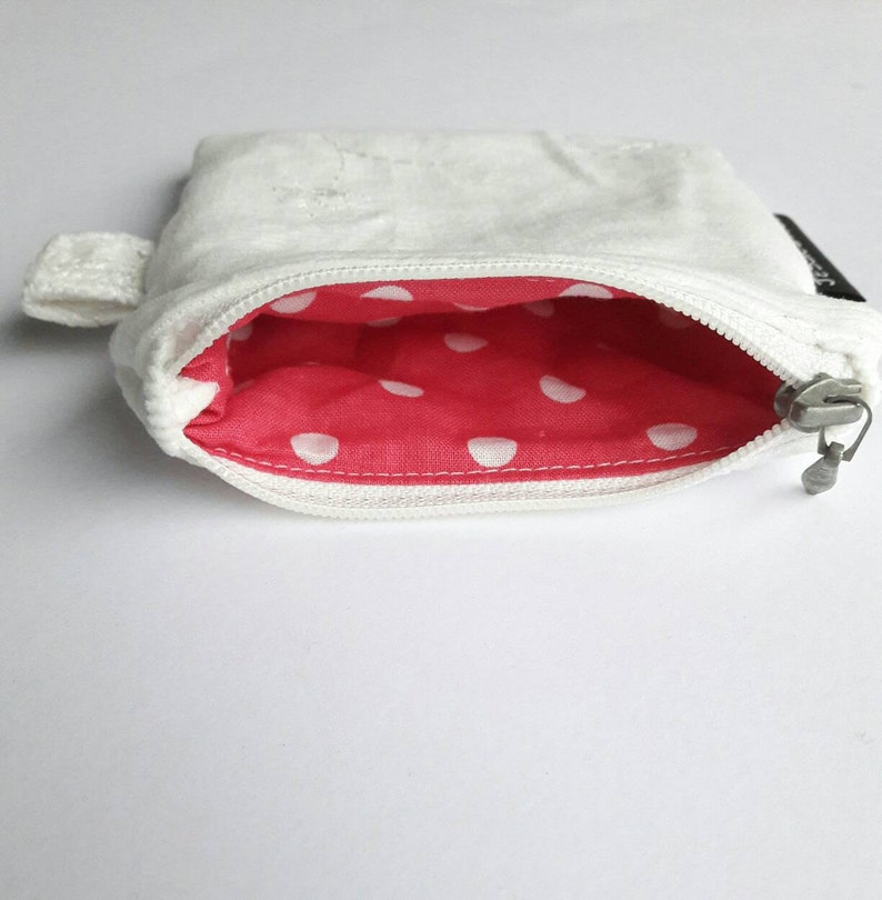 May include: A white zippered pouch with a red and white polka dot lining. The pouch has a small loop handle.