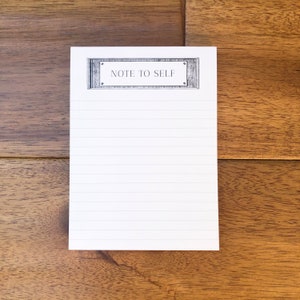 May include: A white notepad with lined paper and a black and white decorative border with the text "Note to Self" at the top.