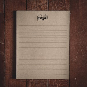 May include: A lined notepad with a brown paper cover and a black and white illustration of a buffalo at the top.