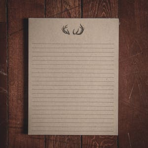 Könnte beinhalten: Ein leeres Blatt liniertes Papier mit einer einfachen Zeichnung von Geweih oben. Das Papier ist braun und hat eine raue Textur. Das Papier liegt auf einer Holzoberfläche.