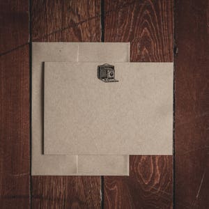 Pode incluir: Dois envelopes marrons com uma ilustração de câmera vintage no envelope superior.