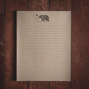 May include: A lined sheet of brown paper with a black and white illustration of a bear and a star at the top.