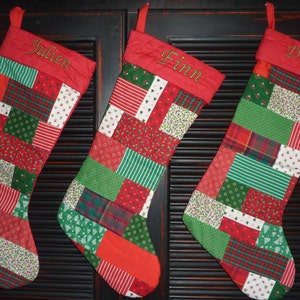 May include: Three red and green patchwork Christmas stockings with the names Julien, Finn, and Drake embroidered on them.