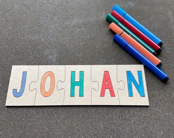 Peut inclure: Un puzzle avec le nom "JOHAN" écrit en lettres colorées. Les lettres sont sur un fond brun clair. Il y a cinq marqueurs multicolores à côté du puzzle.