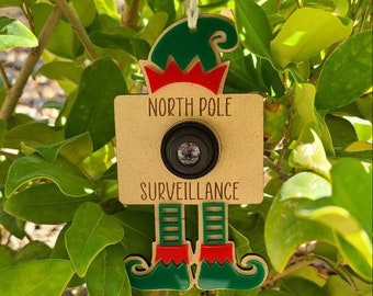 Peut inclure: Une décoration d'elfes en bois avec un objectif d'appareil photo et le texte "Surveillance du pôle Nord".