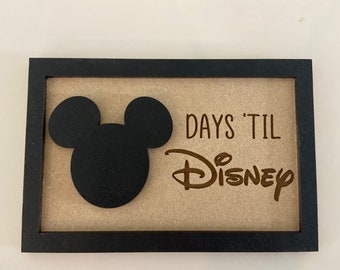 Peut inclure: Un cadre en bois noir avec un fond beige. Le cadre présente une silhouette noire de Mickey Mouse et le texte "DAYS 'TIL DISNEY" en lettres brunes.