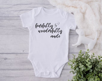 Peut inclure: Combinaison blanche pour bébé avec un texte noir qui dit "fearfully & wonderfully made".