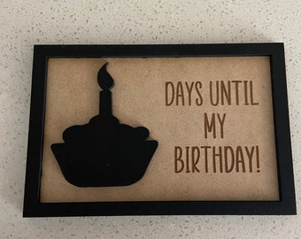 Peut inclure: Une pancarte encadrée de noir avec un fond brun. La pancarte a une silhouette noire d'un cupcake avec une bougie sur le dessus. Le texte sur la pancarte dit "Days Until My Birthday!"