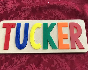 Peut inclure: Une enseigne en bois avec le nom "TUCKER" écrit en lettres colorées. Les lettres sont rouges, bleues, jaunes, vertes, orange et rouges.